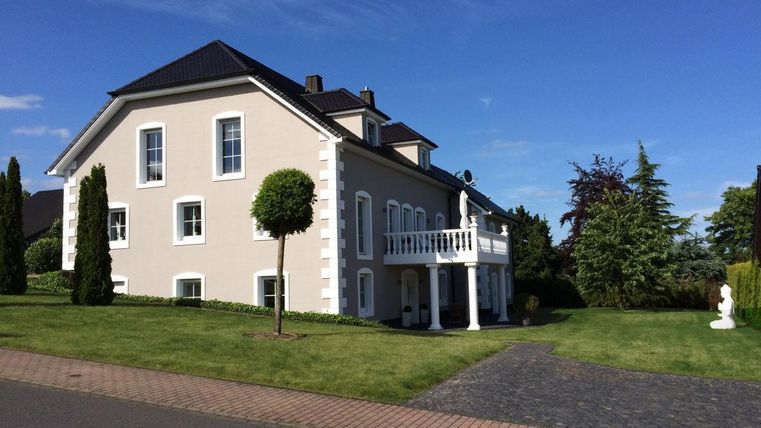 Ein elegantes zweigeschossiges Haus mit einem sauberen Garten und gepflegten Bäumen. Der Himmel ist klar und blau, was eine schöne Atmosphäre schafft.