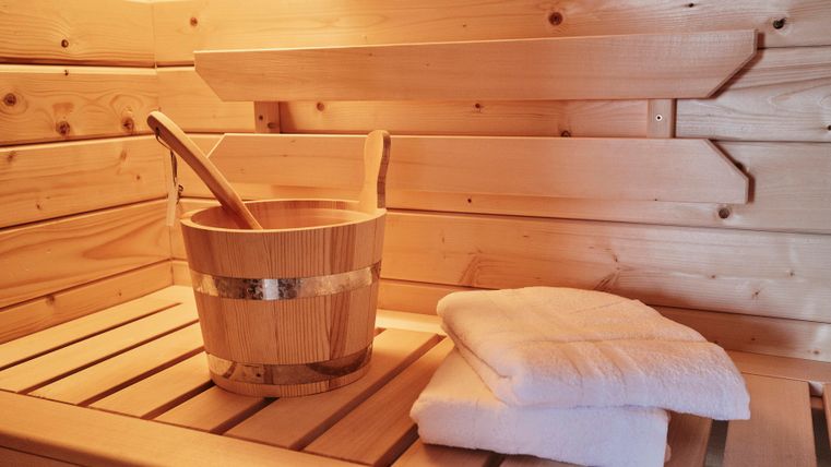 Ein beruhigender Saunabereich aus Holz mit einer Holzschüssel und zwei sauberen Handtüchern. Die warme Atmosphäre lädt zur Entspannung ein.