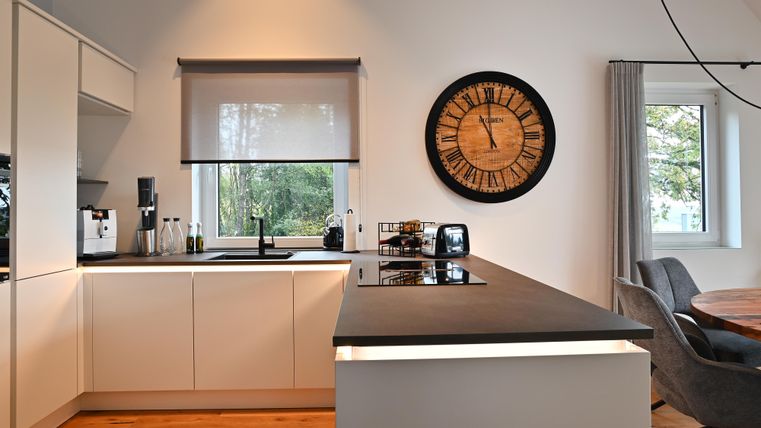 Moderne Küche mit Kücheninsel und Holzoberfläche. Große Fenster sorgen für viel natürliches Licht.