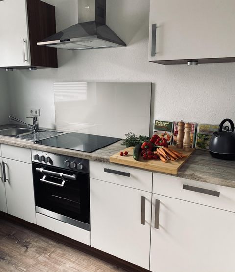 Eine moderne Küche mit weißen Schränken und einer edlen Arbeitsplatte. Auf dem Tisch sind frisches Gemüse und Küchenutensilien sichtbar.