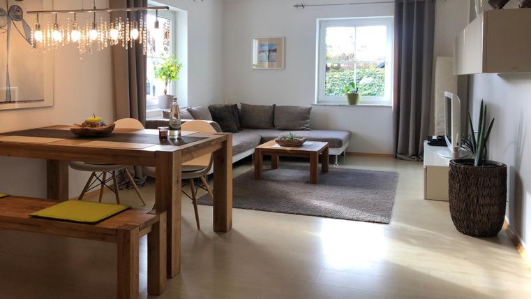 Ein modernes Wohnzimmer mit einer bequemen Couch und einem Esstisch. Große Fenster sorgen für viel Tageslicht und eine angenehme Atmosphäre.