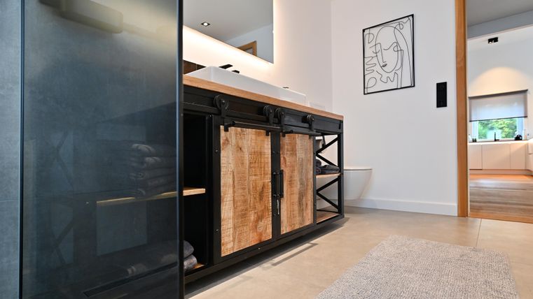 Ein modernes Badezimmer mit einem stilvollen Waschtisch aus Holz und Metall. Der Glanz des Raumes wird durch das natürliche Licht und die minimalistischen Formen betont.