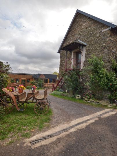 Un bâtiment historique en pierre avec un escalier. Au premier plan, il y a une vieille charrette avec des fleurs.