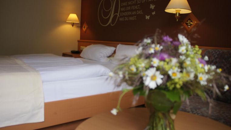 Ein gemütliches Hotelzimmer mit einem Doppelbett und sanfter Beleuchtung. Auf dem Tisch steht eine Vase mit bunten Blumen.