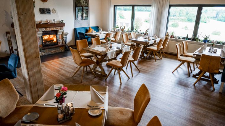 Een gezellig restaurant met houten tafels en stoelen. De open haard zorgt voor een warme sfeer en grote ramen bieden uitzicht op het groen.