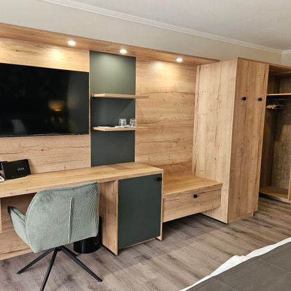 Ein modernes Hotelzimmer mit einem Holzregal, einem Schreibtisch und einem Fernseher. Der Raum ist hell und einladend gestaltet.