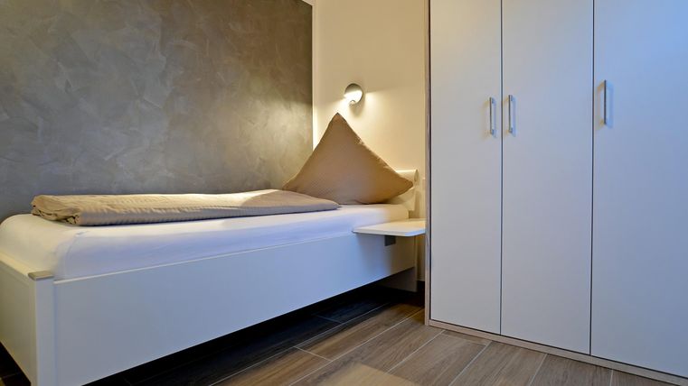 Ein einfaches, modernes Zimmer mit einem Einzelbett und einem Schrank. Die Wände sind neutral gestaltet und das Licht ist sanft.