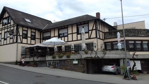 Ein traditionelles Fachwerkhaus mit einer Terrasse und Sonnenschirmen. Es befindet sich an einer Straße und hat moderne Autos davor geparkt.