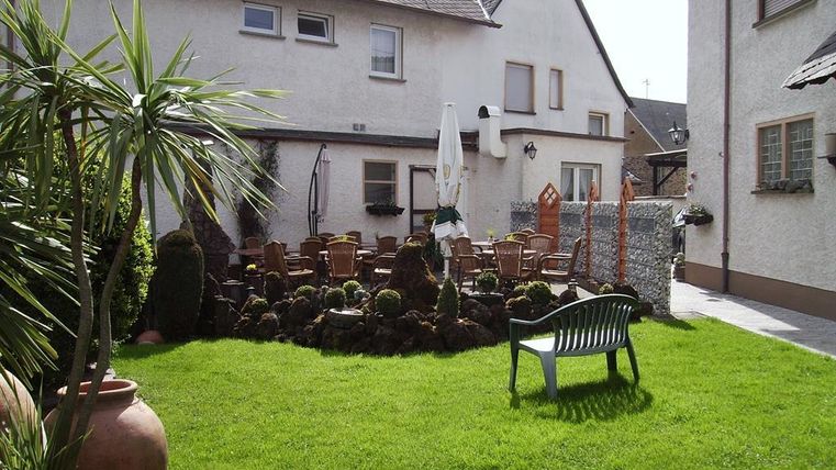 Een uitnodigende tuin met groene gras en gezellige zitplaatsen. Op de achtergrond staan meerdere gebouwen en een parasol.