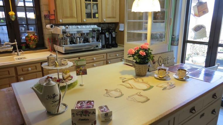 Eine gemütliche Küche mit Holzschränken und einer großen Kochinsel. Auf der Arbeitsplatte stehen Blumen und Teekannen, daneben ist eine Kaffeemaschine.