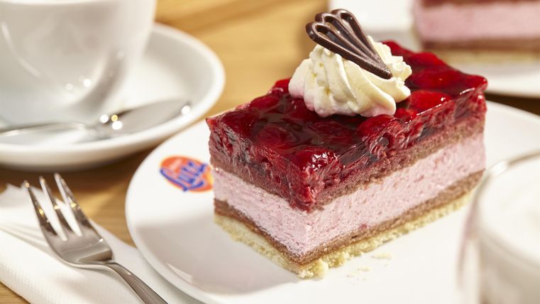 Ein leckerer Kuchen mit mehreren Schichten aus Sahne und Früchten. Dazu gibt es eine Tasse Kaffee im Hintergrund.