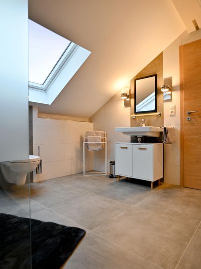 A modern bathroom with a large window area and a bright wood decor. It features a stylish sink cabinet and a separate toilet.