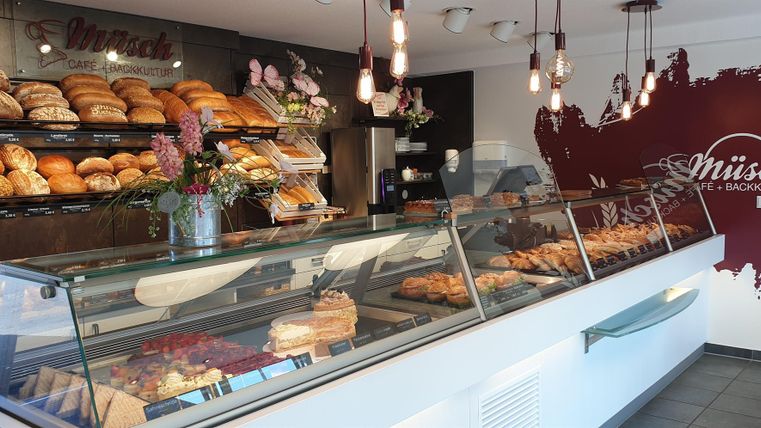 Eine Bäckerei mit frischen Brötchen und Gebäck in der Vitrine. Im Hintergrund sind zahlreiche Brote und eine decorative Wandgestaltung zu sehen.