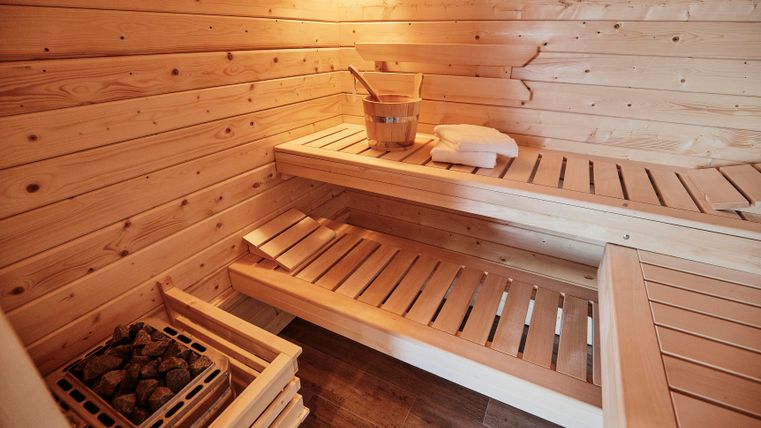 Eine warme Sauna mit Holzbänken und einem Eimer. Entspannung und Wohlbefinden stehen im Mittelpunkt.