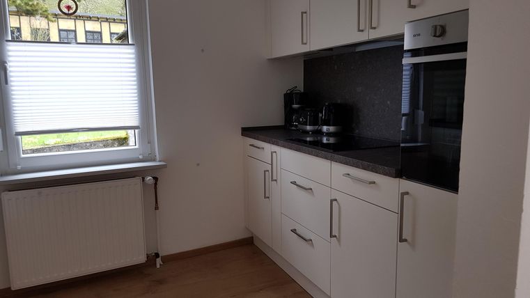 Eine moderne Küche mit weißen Schränken und einem schwarzen Arbeitsplatten. Das Fenster lässt viel Tageslicht herein.