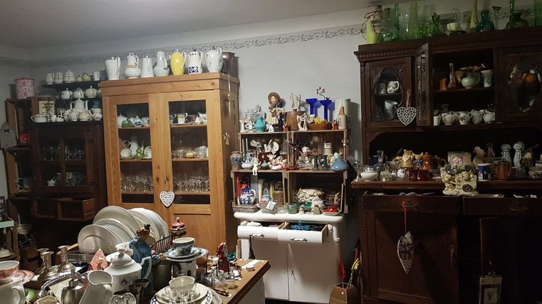 Ein Raum voller antiker Sammlerstücke und Geschirr. Regale sind mit Gläsern, Porzellan und kleinen Dekorationsgegenständen gefüllt.