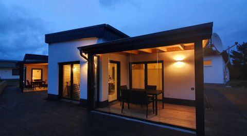 Ein modernes Haus mit einem überdachten Außenbereich, beleuchtet in der Dämmerung. Der offene Raum bietet Sitzgelegenheiten und einen Blick nach draußen.