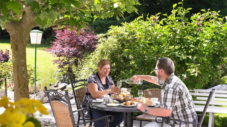 Ein schönes Essen im Freien unter einem Baum. Zwei Personen genießen ihr Essen und stoßen mit Gläsern an.