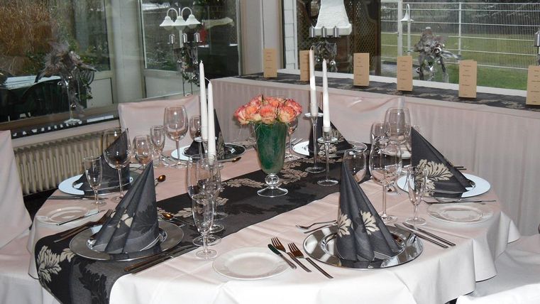 Ein elegant gedeckter Tisch mit schwarzer Tischdecke, Gläsern und Besteck. In der Mitte steht eine vase mit frischen Blumen.