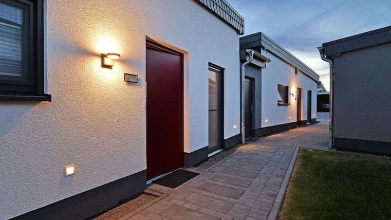 Eine moderne Wohnanlage mit hellen Fassaden und einem gepflasterten Weg. Die Gebäude sind in sanften Farben gehalten und mit Außenbeleuchtung versehen.