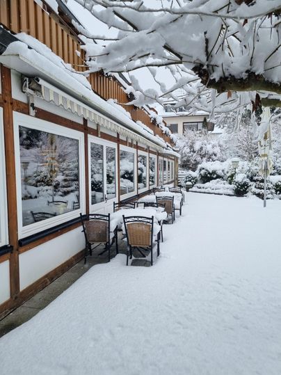 Ein schneebedecktes Café mit Tischen und Stühlen im Freien. Die Umgebung ist malerisch und winterlich.