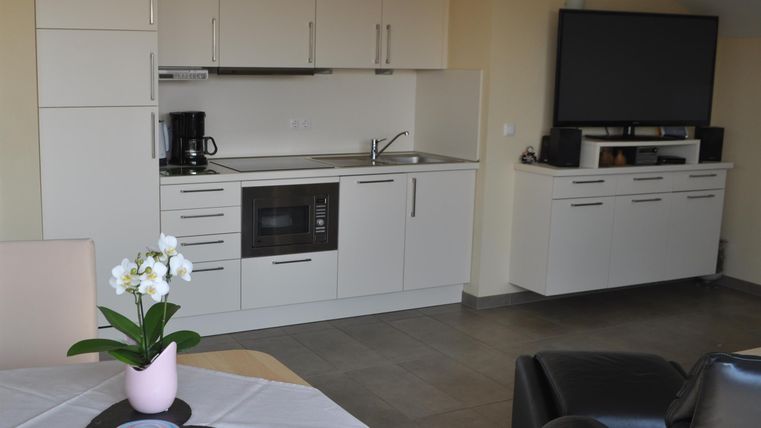 Eine moderne Küche mit weißen Schränken und einem integrierten Kochfeld. Im Vordergrund steht ein Tisch mit einer Vase und einer Pflanze.