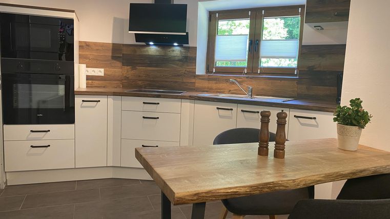 Eine moderne Küche mit weißen Schränken und einer Holzarbeitsplatte. Der Essbereich ist mit einem Holztisch und zwei Stühlen ausgestattet.