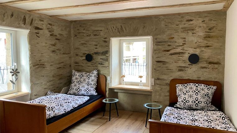 Ein gemütliches Schlafzimmer mit zwei Betten und modernem Design. Die Wände sind mit Naturstein verkleidet, und es gibt große Fenster für viel Tageslicht.