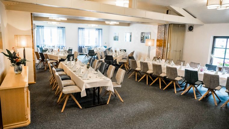 Een elegante evenementruimte met gedekte tafels en stoelen. Zachte verlichting en grote vensters creëren een uitnodigende sfeer.