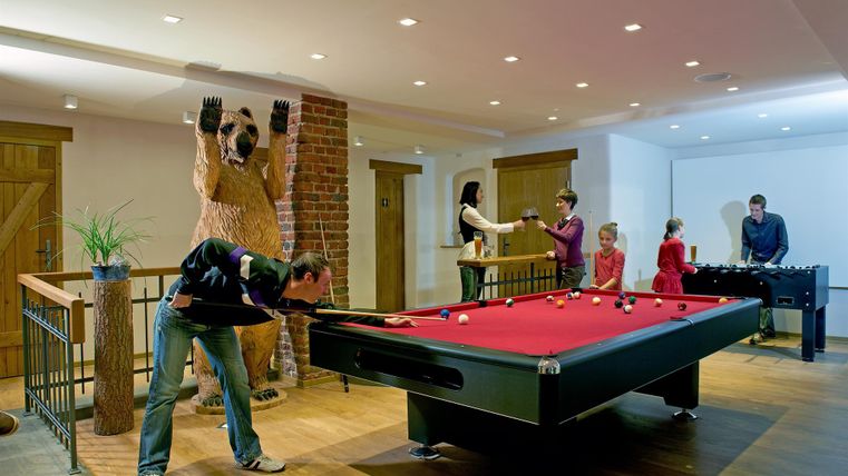 Ein Freizeitbereich mit einem Billardtisch und einem Foosballtisch. Eine Gruppe von Menschen spielt und steht in einer gemütlichen Atmosphäre.