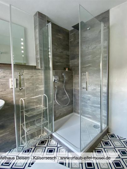 Eine moderne Dusche aus Glas mit grauen Fliesen und einem eleganten Design. Der Raum ist hell und einladend gestaltet.