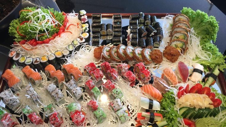 Eine platte mit einer Vielzahl von Sushi-Sorten, darunter Nigiri, Maki und Sashimi. Frisches Gemüse und Salatblätter sind dekorativ angeordnet.
