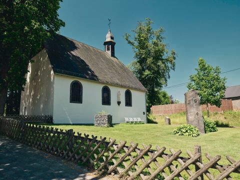 Eine kleine Kirche steht inmitten einer grünen Landschaft. Umgeben von einem gepflegten Garten und einem Zaun aus Holz.
