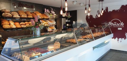 Eine Bäckerei mit frischen Brötchen und Gebäck in der Vitrine. Im Hintergrund sind zahlreiche Brote und eine decorative Wandgestaltung zu sehen.