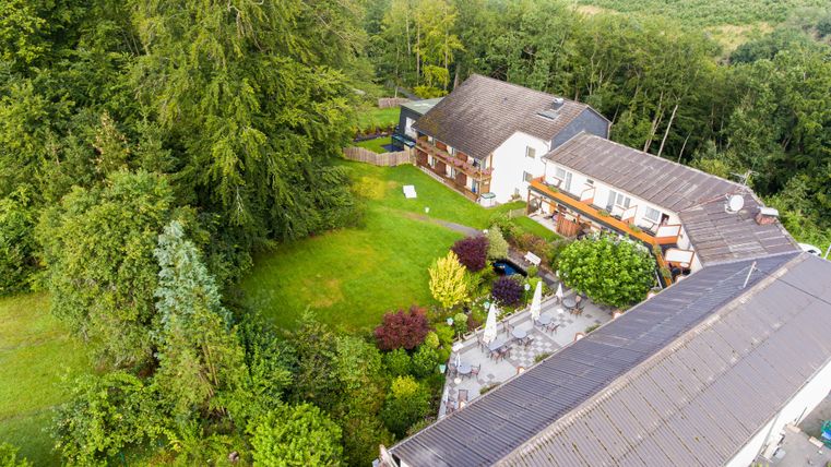 Ein malerisches Anwesen umgeben von grünen Bäumen und einem Garten. Das Gebäude hat mehrere Stockwerke und eine einladende Terrasse.