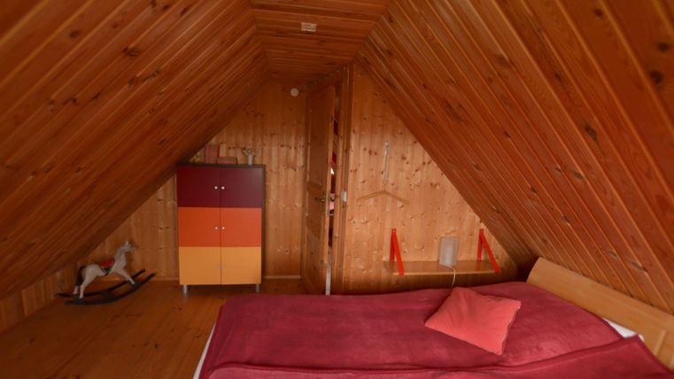 Une chambre mansardée confortable avec des murs en bois et un plafond bas. La chambre est équipée d'un grand lit et d'une armoire colorée.