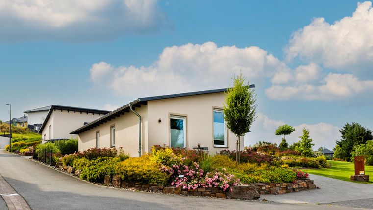 Eine moderne Wohnsiedlung mit ansprechend gestalteten Gärten. Im Hintergrund sind sanfte Hügel und ein blauer Himmel zu sehen.