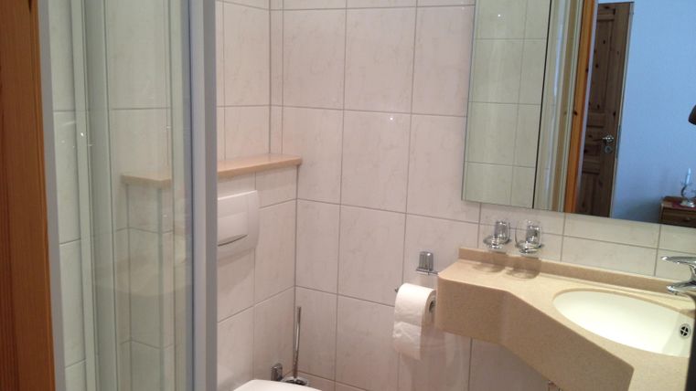 Ein Badezimmer mit Dusche, Toilette und Waschbecken. Die Wände sind gefliest und der Raum wirkt hell und sauber.