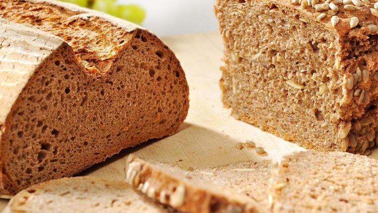 Ein angenehm angerichtetes Brot aus Vollkorn mit Sesam, in Scheiben geschnitten. Im Hintergrund sind grüne Weintrauben sichtbar.