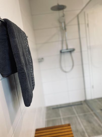 Ein modernes Badezimmer mit einer Dusche und einem Handtuch. Der Boden ist mit grauen Fliesen ausgestattet.