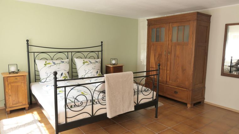 Ein gemütliches Schlafzimmer mit einem schmiedeeisernen Bett und bunten Kissen. Es gibt einen Holzschrank und einen Nachttisch, die einen warmen, einladenden Eindruck vermitteln.