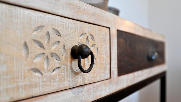 Ein rustikaler Tisch mit geschnitzten Schubladen und Metallgriffen. Die Oberfläche hat eine helle, verwitterte Optik.