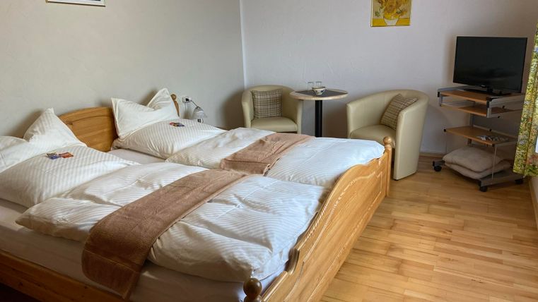 Een gezellige slaapkamer met twee bedden en een houten vloer. Er staat een kleine tafel en stoelen, evenals een tv in de hoek.