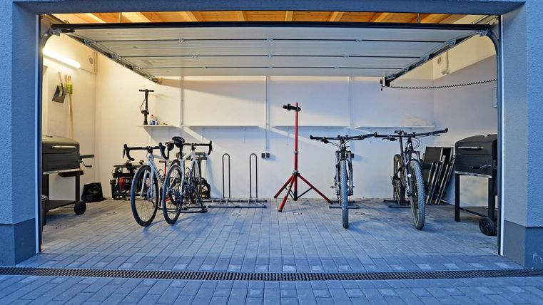 Eine saubere Garage mit zwei Fahrrädern und Werkzeug. Im Hintergrund stehen weitere Fahrräder und ein Grill.