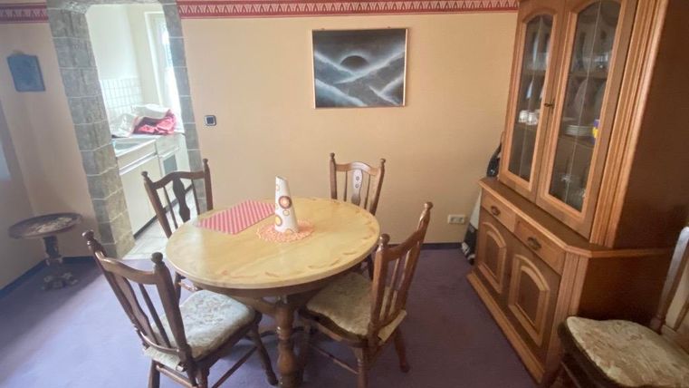 Ein gemütlicher Essbereich mit einem runden Tisch und Stühlen. Im Hintergrund steht ein Holzschrank und es gibt einen Zugang zur Küche.