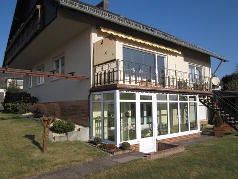 Ein gemütliches Haus mit einem Balkon und einem Wintergarten. Der Garten ist gepflegt und bietet eine einladende Atmosphäre.