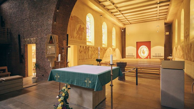 Eine ruhige Kirche mit einem einfachen Altar und bunten Fenstern. Die Wände sind mit historischen Fresken dekoriert.