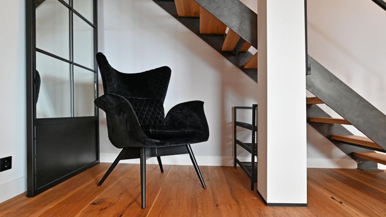 Ein eleganter schwarzer Stuhl steht in einem modernen Raum. Im Hintergrund ist eine Treppe mit Holzstufen sichtbar.