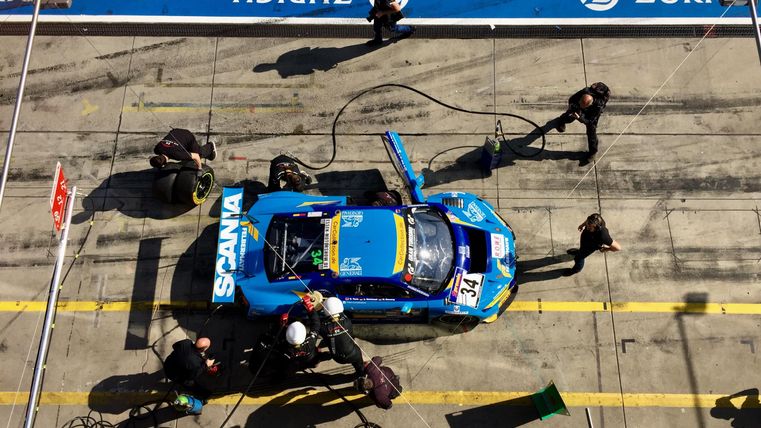 Ein Rennwagen wird in der Boxengasse gewartet. Mehrere Techniker arbeiten konzentriert daran, ihn für das Rennen vorzubereiten.