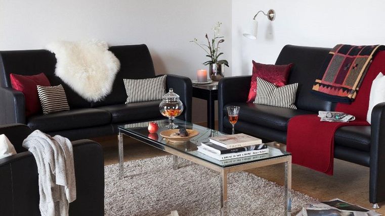 Une conception de salon confortable avec des canapés noirs et des coussins décoratifs. Sur la table, il y a des livres, une bougie parfumée et un verre avec une boisson.